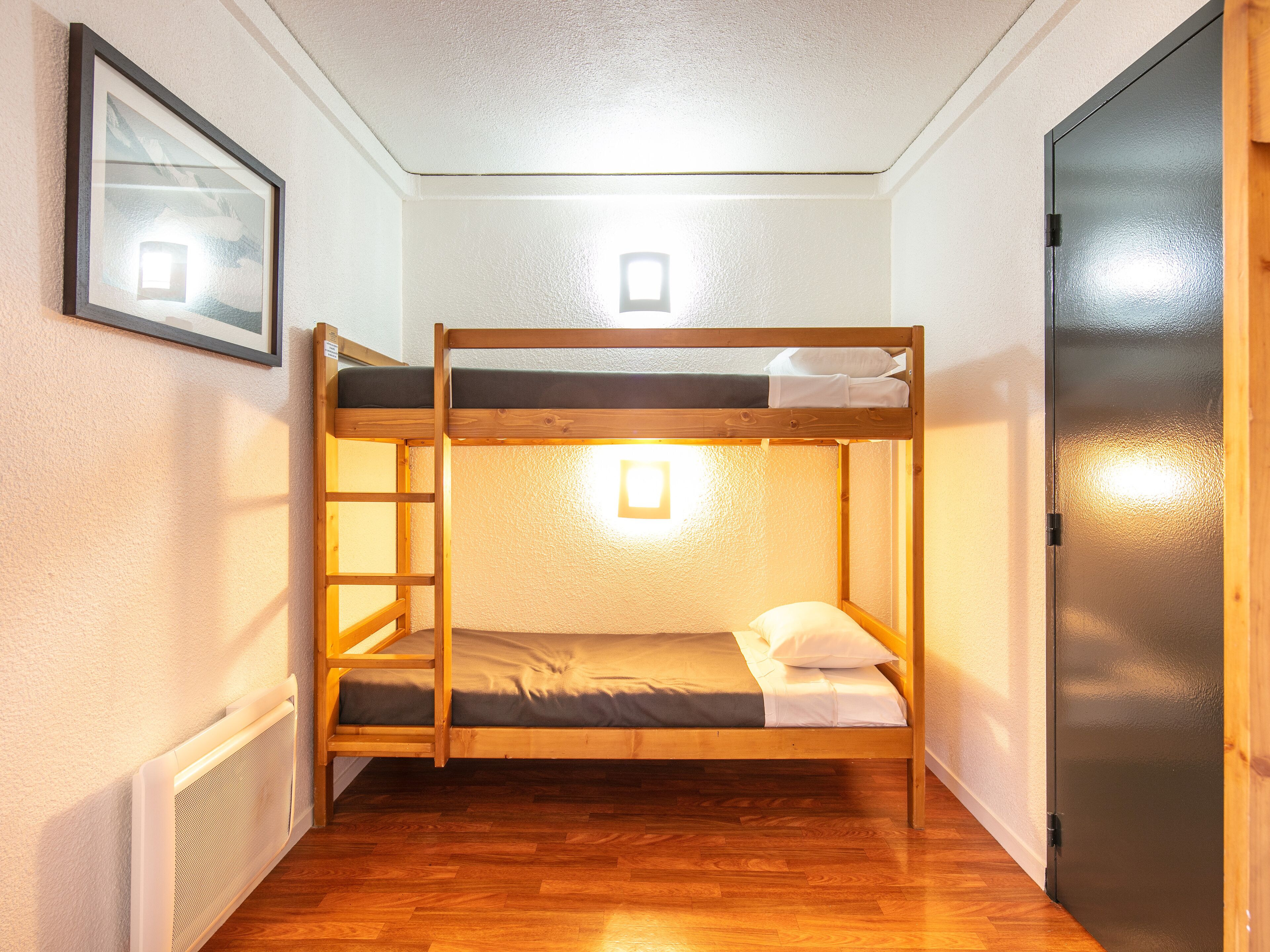 A bunk bed room with a ladder, a door, and a framed picture on the wall.