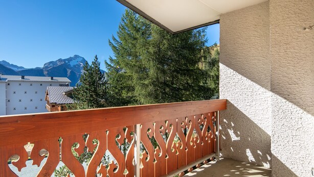 Een balkon met een houten leuning en uitzicht op bergen en bomen.