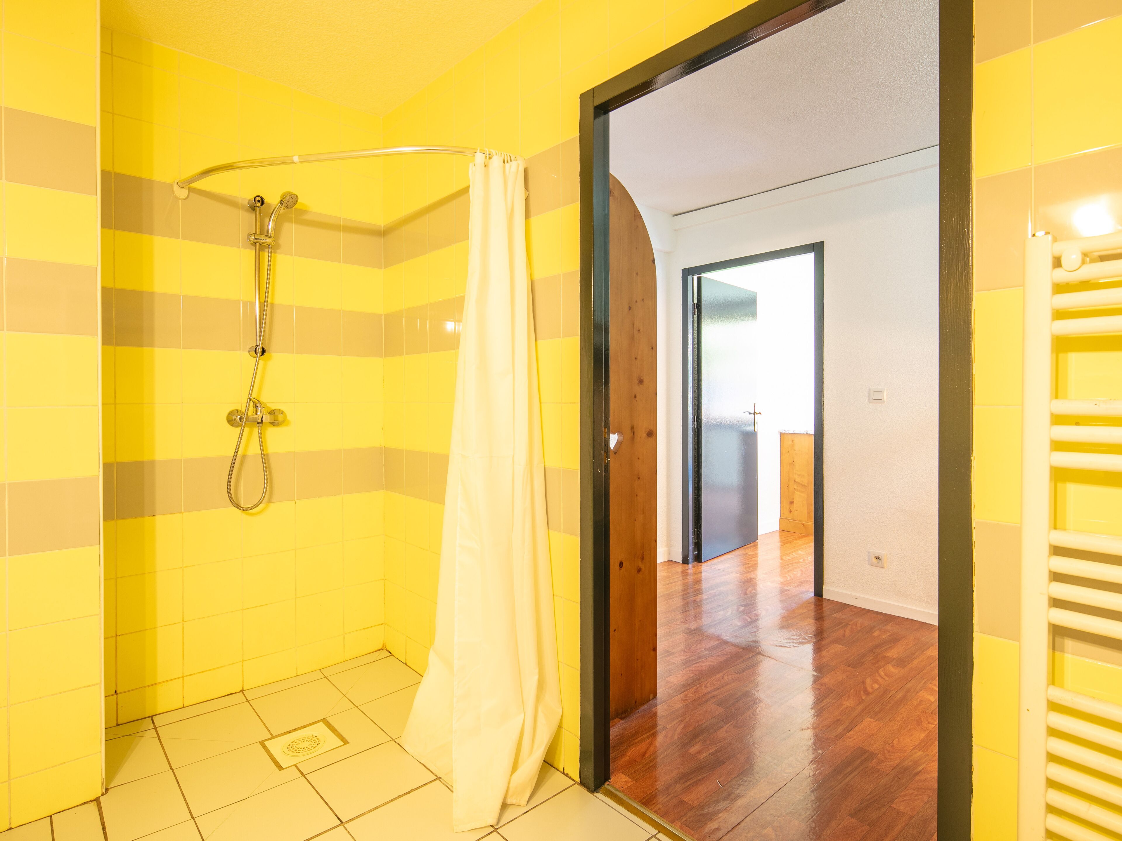 A bathroom with yellow tiles, a shower, and a wooden door leading to another room.