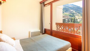 Een slaapkamer met een bed, een raam met uitzicht op het landschap en een houten balkonhek.