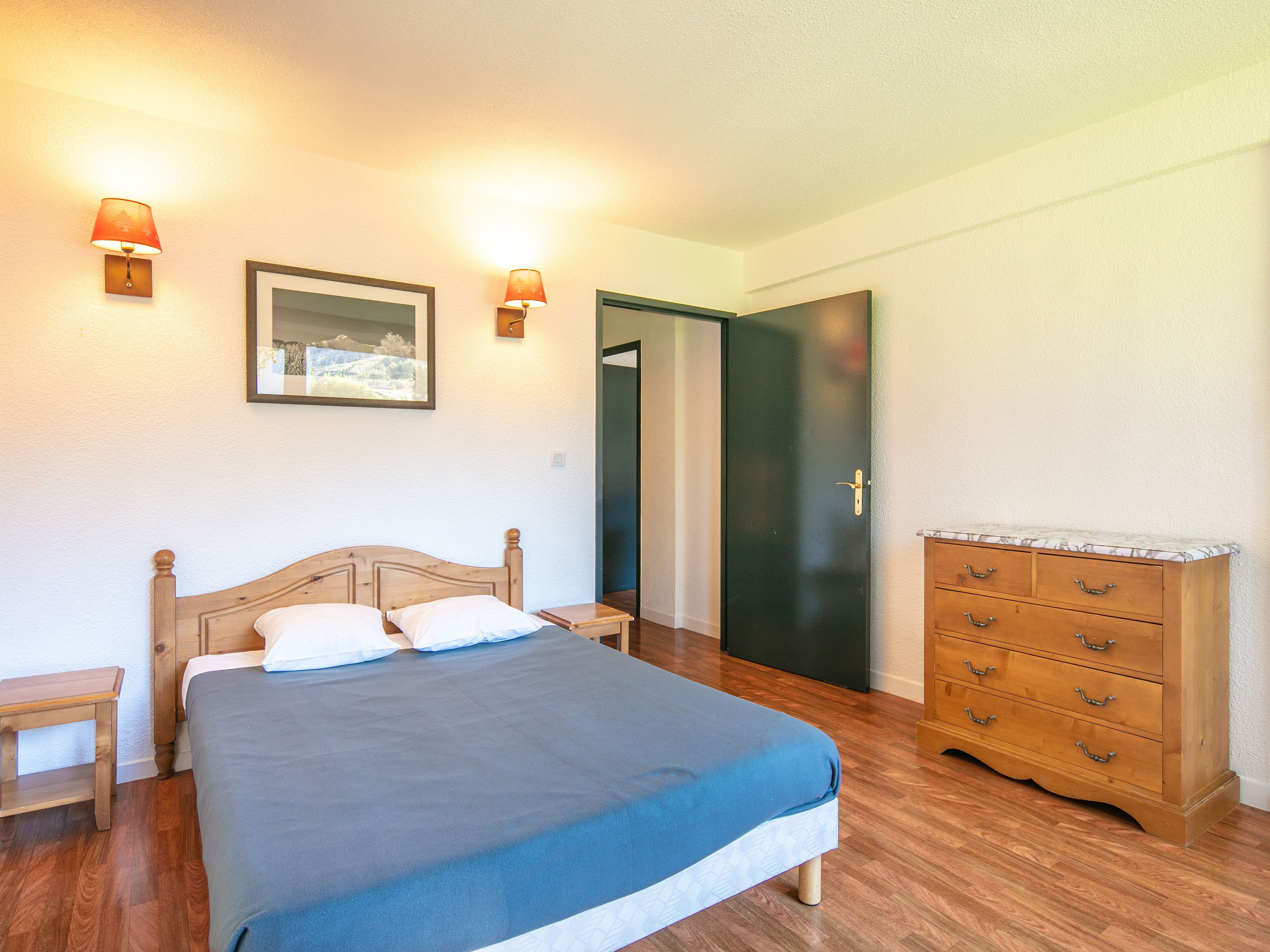 A bedroom with a bed, bedside tables, a dresser, and two wall-mounted lamps.