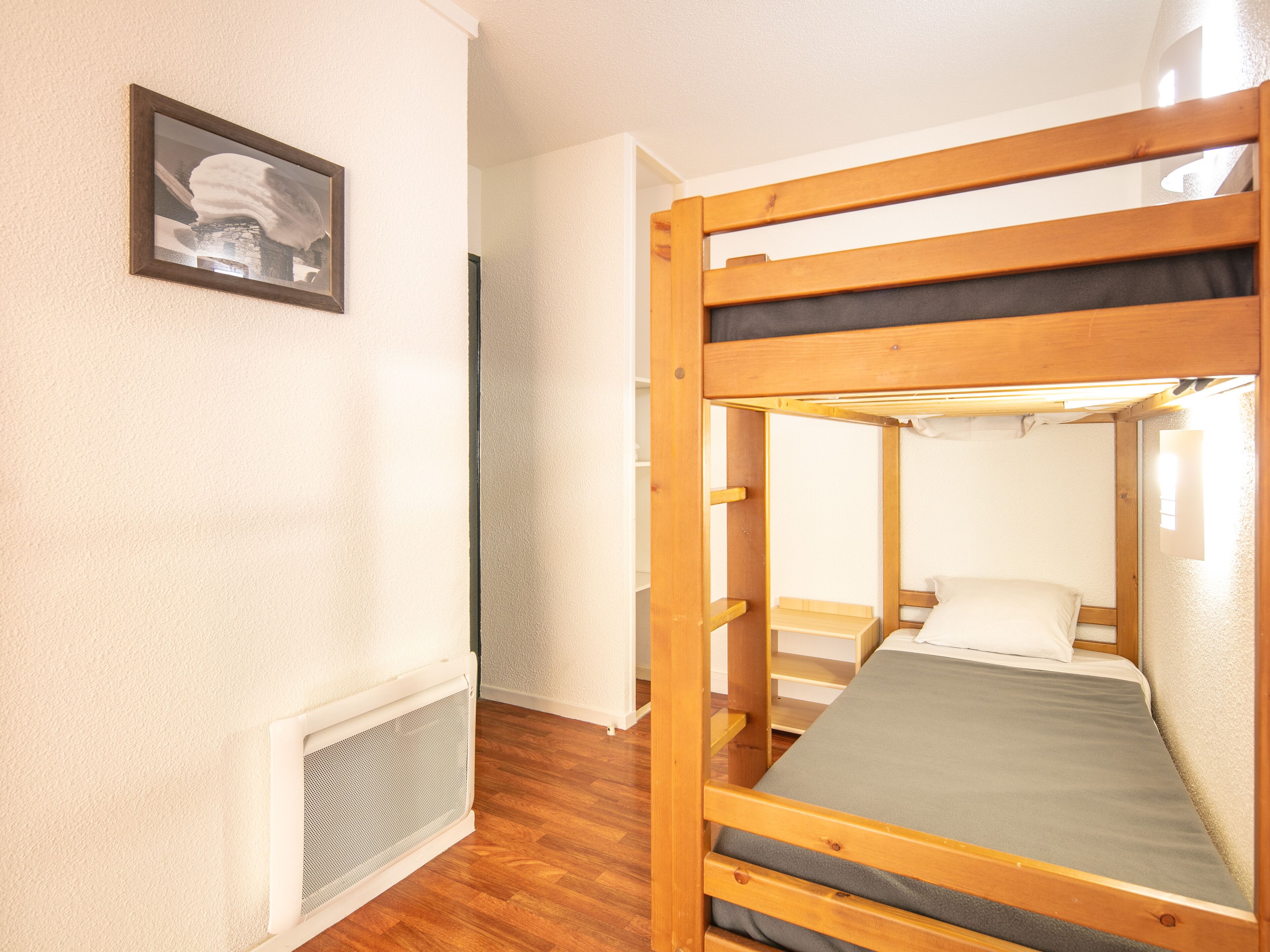 Un lit superposé avec un matelas et des oreillers, un radiateur et un tableau encadré au mur.