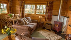 A cozy log cabin interior with a leather sofa, a dining table with chairs, a fireplace, and a window with curtains. - Stable Lodge (Glasgow)