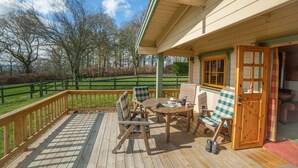 A wooden deck with outdoor seating, a table, and a door leading to a room. - Stable Lodge (Glasgow)