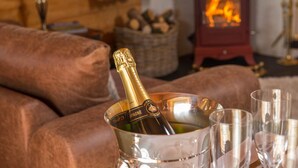 A cozy living room with a fireplace, a sofa, and a champagne bottle in a glass. - Stable Lodge (Glasgow)