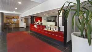 A reception area with a red counter, a large potted plant, and a wooden wall with a sign that reads "Business Center".