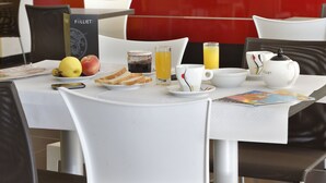 A breakfast table with a book, fruit, juice, and a coffee pot.