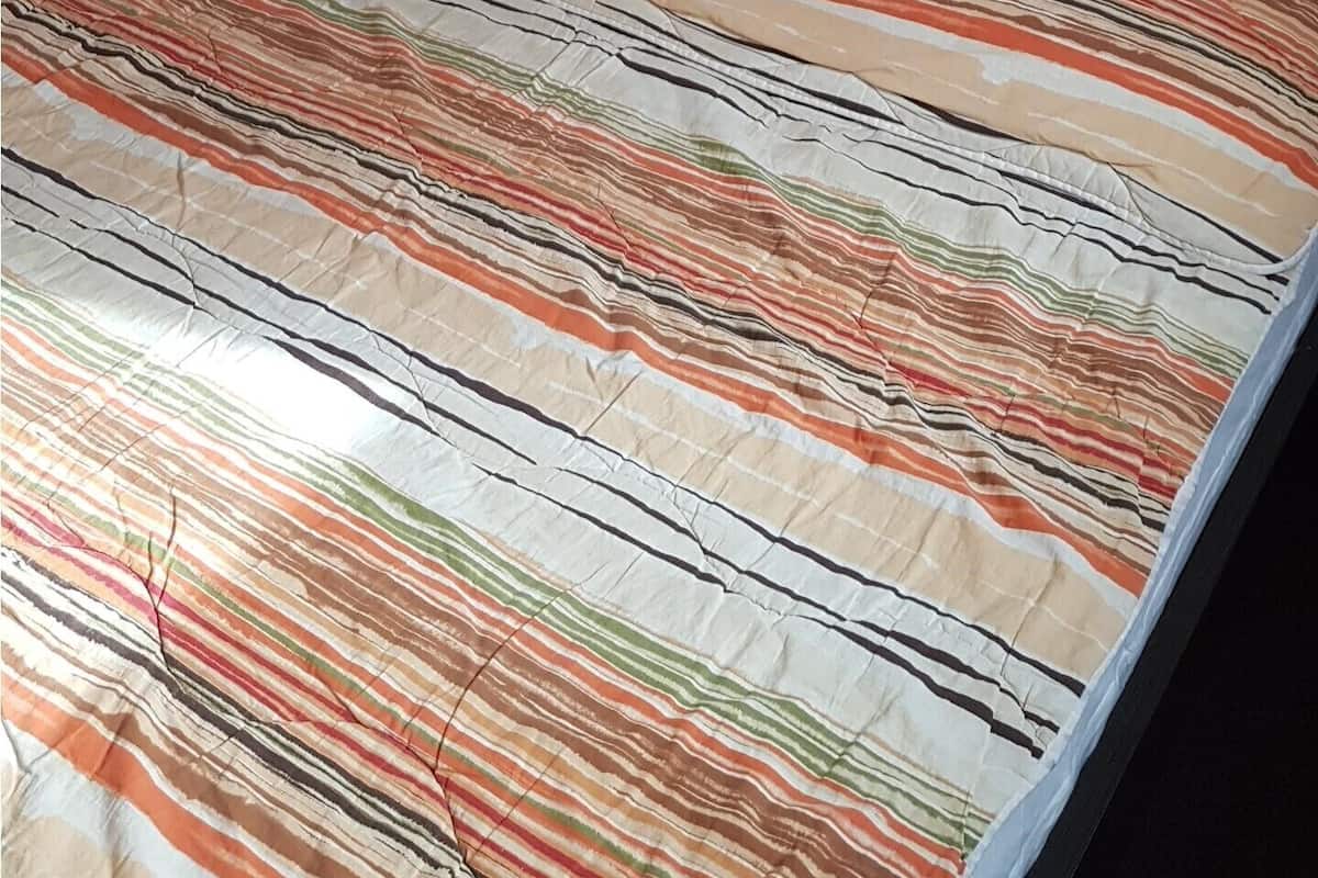 A neatly made bed with a striped bedspread, a bedside lamp, and a framed abstract painting on the wall.