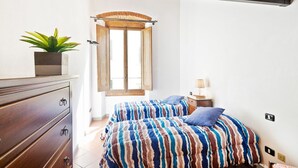 Un dormitorio con dos camas, un aparador de madera, una planta en maceta y una ventana con cortinas.