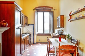 Une cuisine avec des meubles de rangement en bois, une fenêtre, une table à manger avec des chaises et un four à micro-ondes.