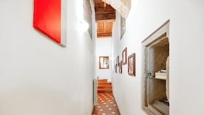 Un pasillo estrecho con piso de baldosas, una escalera de madera y cuadros en las paredes.