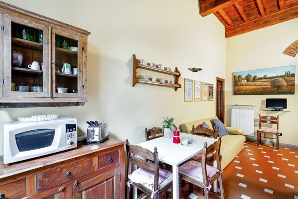 A rustic kitchen with a microwave, toaster, wooden cabinets, and a dining table with chairs.