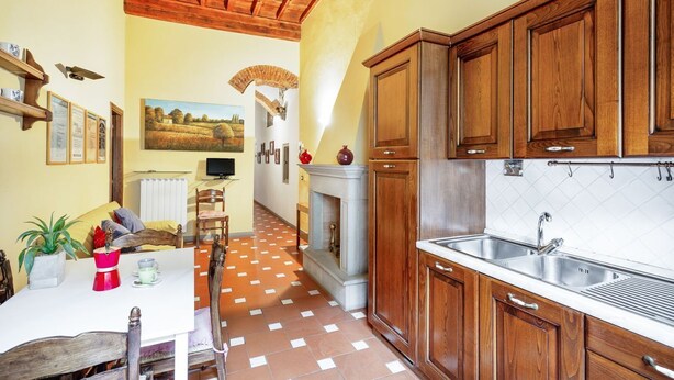 Una cocina con armarios de madera, suelo de baldosas, chimenea y comedor con mesa y sillas.