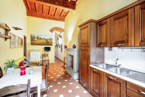 A kitchen with wooden cabinets, a tiled floor, a fireplace, and a dining area with a table and chairs.