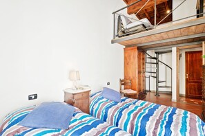 A bedroom with a bed, a nightstand, a lamp, a chair, and a wooden wardrobe.