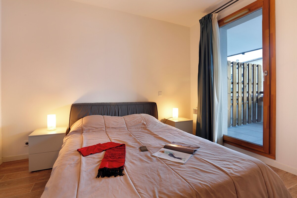 A neatly made bed with a red throw, a bedside lamp, and a magazine on the bed.