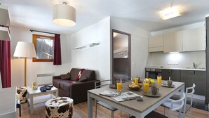 A modern hotel room with a dining area, a sofa, a lamp, and a view of the outside. - Vacanceole - Au Coeur des Ours (Les Deux Alpes)