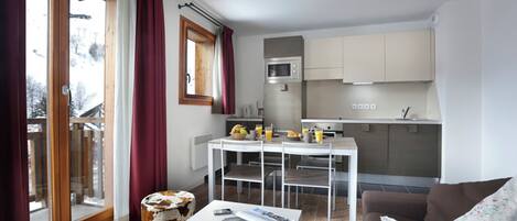 Un salon moderne avec une table basse blanche, un canapé marron et un coin repas comprenant une table et des chaises blanches.