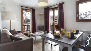 A modern hotel room with a sofa, dining table, and breakfast setup. - Vacanceole - Au Coeur des Ours (Les Deux Alpes)