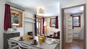 A modern kitchen with a dining table, chairs, and breakfast items. There are windows with curtains, a lamp, and a view of trees outside. - Vacanceole - Au Coeur des Ours (Les Deux Alpes)
