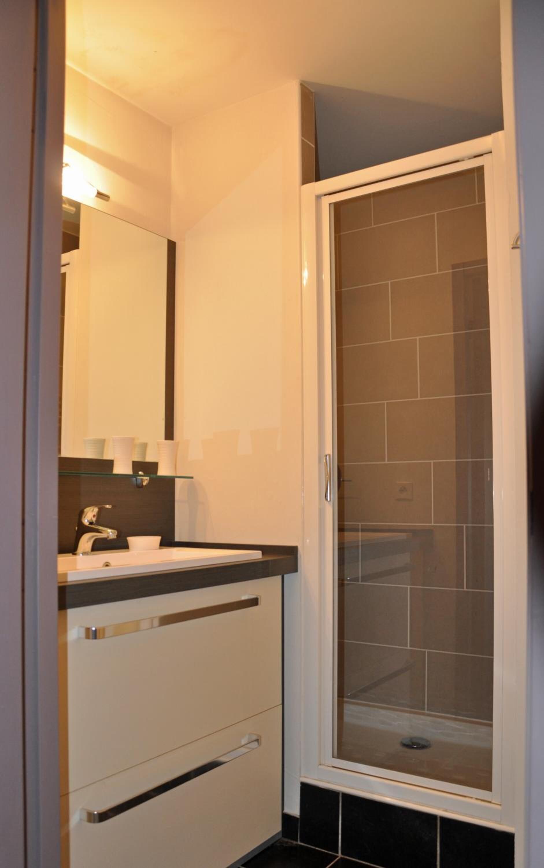 Une salle de bain avec une douche à parois de verre, un lavabo avec un miroir et un meuble avec des tiroirs.