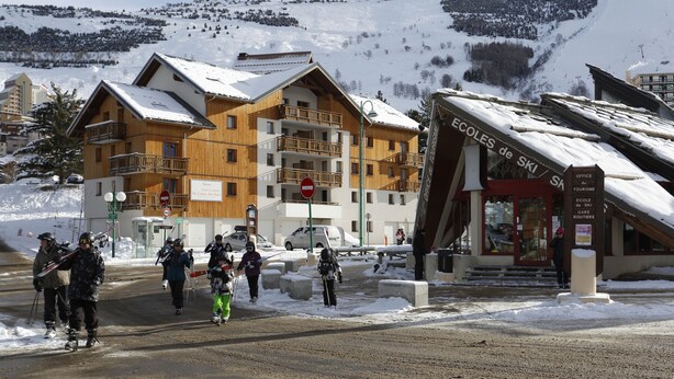 A ski resort with wooden buildings, a ski office, and a sign for ski schools. - Vacanceole - Au Coeur des Ours (Les Deux Alpes)