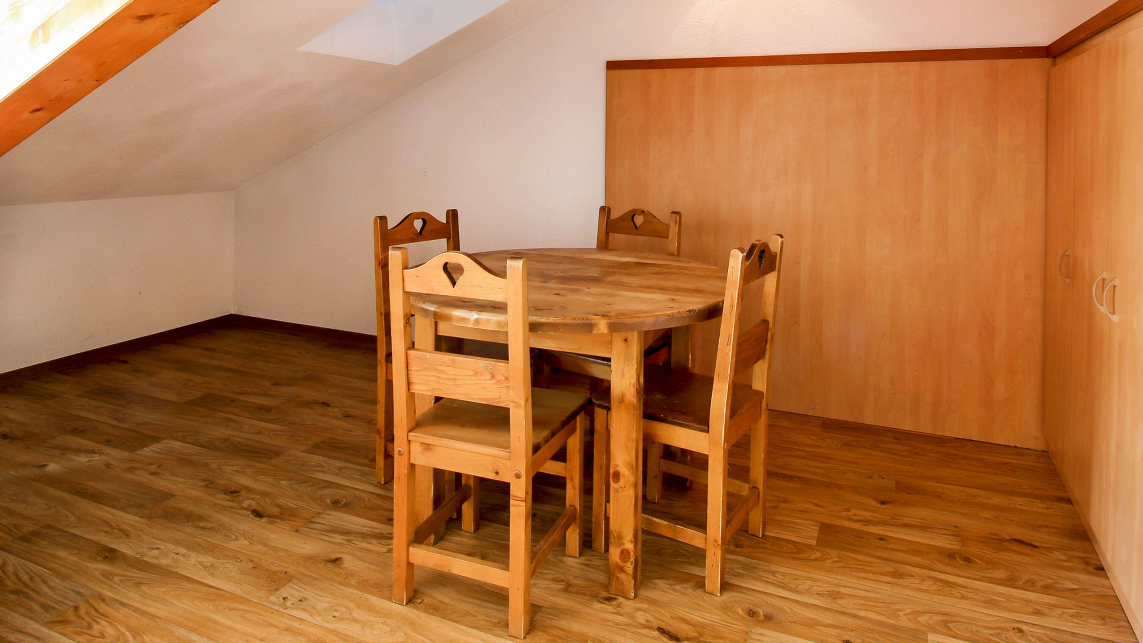 A wooden dining table with chairs in a room with wooden flooring and a sloped ceiling.