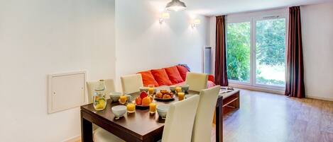 A dining area with a wooden table, white chairs, and a red sofa. There are bowls, glasses, and a bottle on the table.