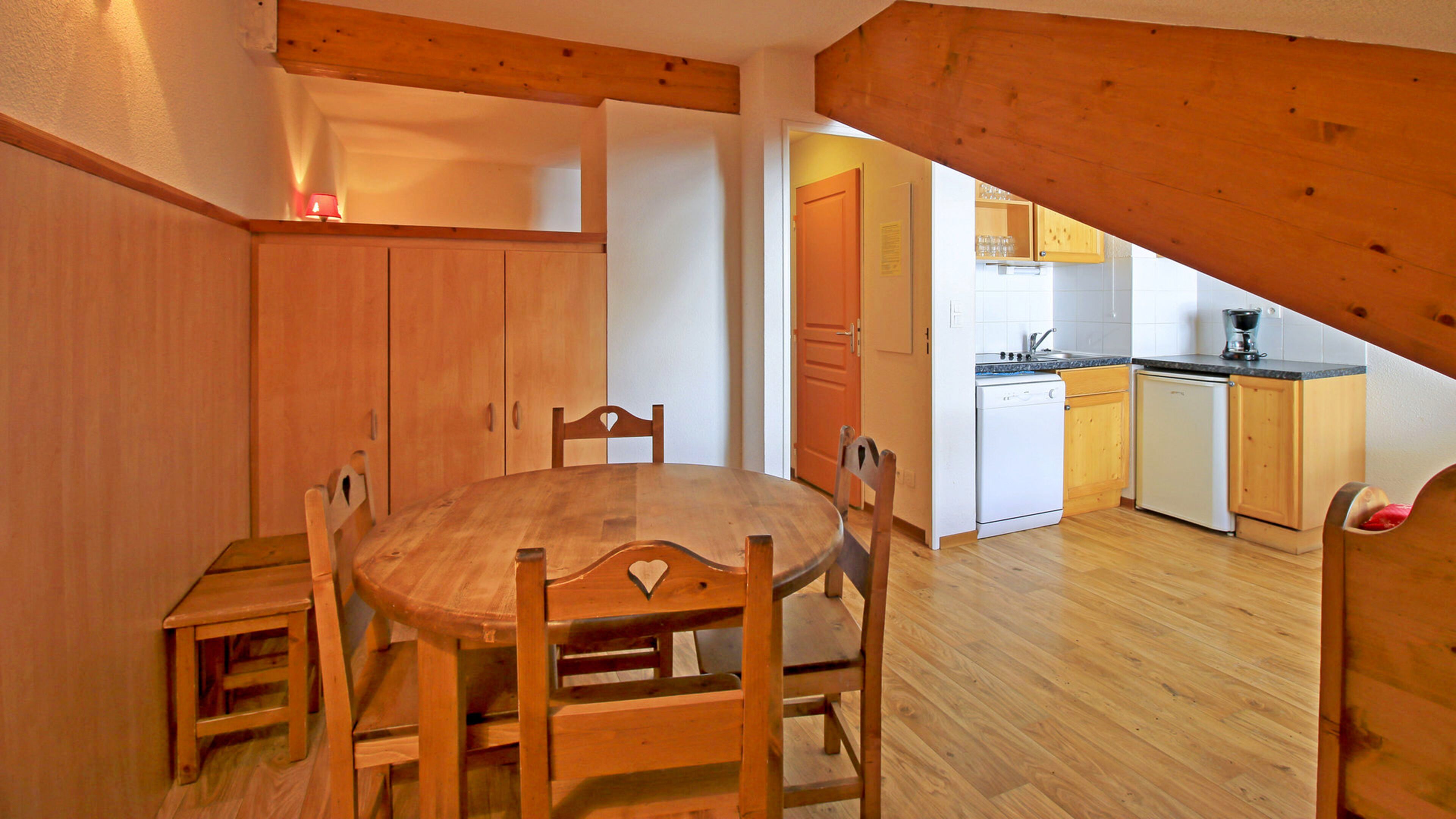 A dining area with a wooden table and chairs, a kitchen with wooden cabinets and appliances, and a sloped ceiling.