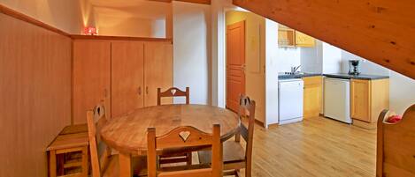 A dining area with a wooden table and chairs, a kitchen with wooden cabinets and appliances, and a sloped ceiling.