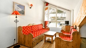 Una habitación acogedora con sofá y sillas de madera, una mesita, una lámpara y una ventana con vistas a un paisaje nevado.