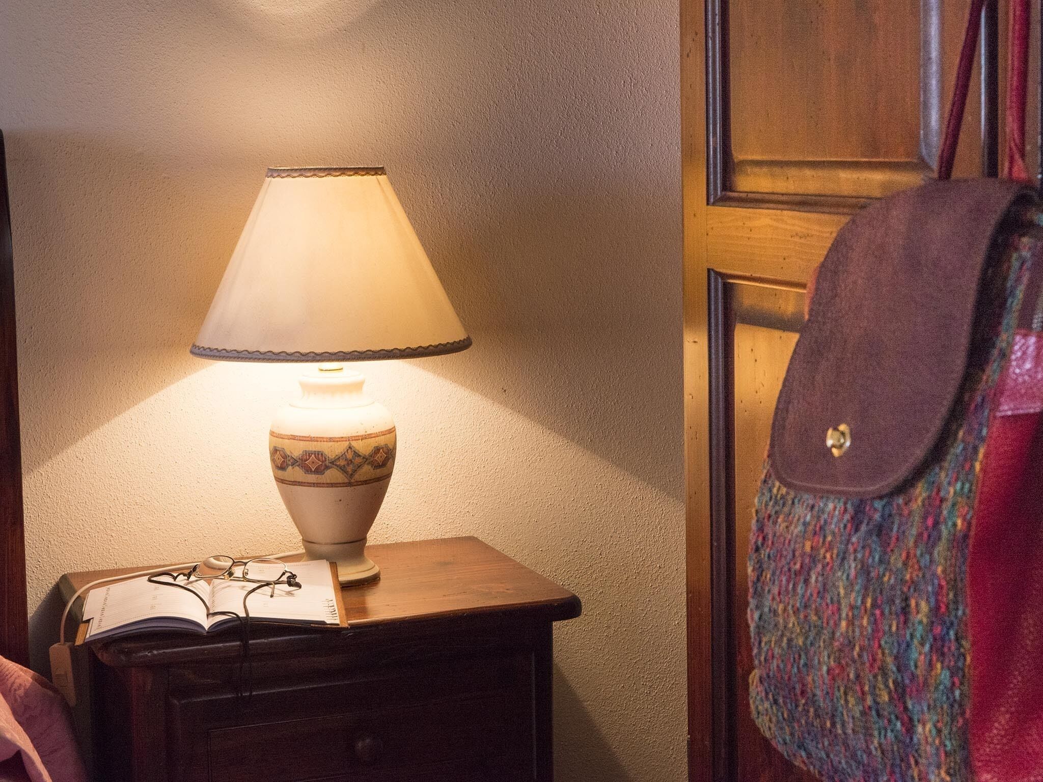 Een nachtkastje met een lamp, een boek en een bril.