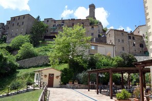 A courtyard with stone steps leading to a small building, surrounded by lush greenery and stone buildings in the background. - Country House il Ciliegio (Roccastrada)