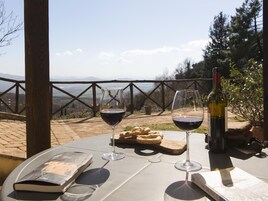 Una mesa con dos copas de vino, una botella y un libro en una terraza con vistas.