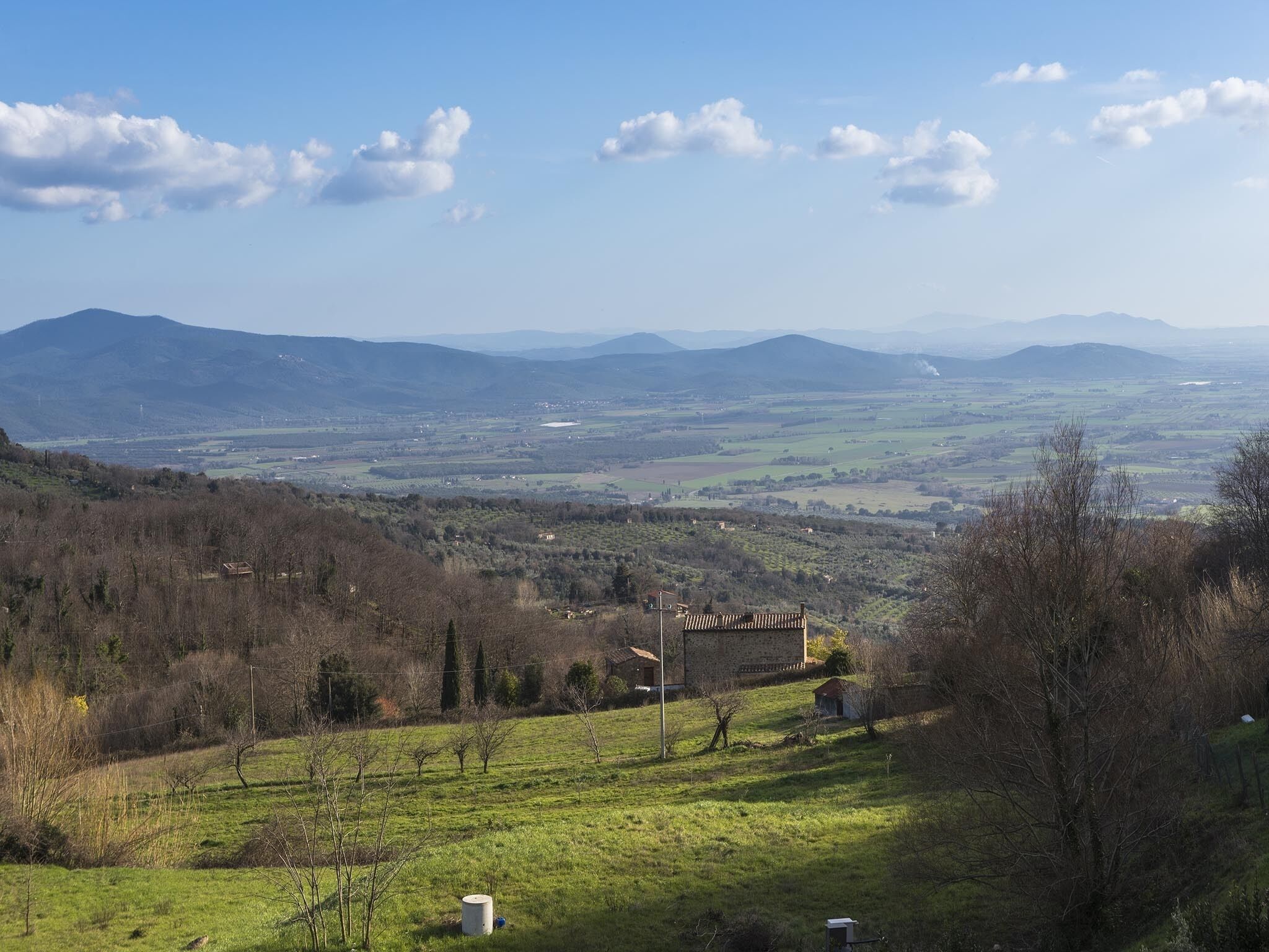 Un paysage rural avec des collines douces, un petit bâtiment en pierre et un ciel bleu dégagé.