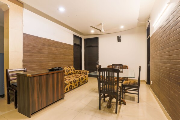 A modern living room with a sofa, a dining table, and chairs. - Via Hemkunt Mansion - Nr Noida Sector-15 Metro (Noida)