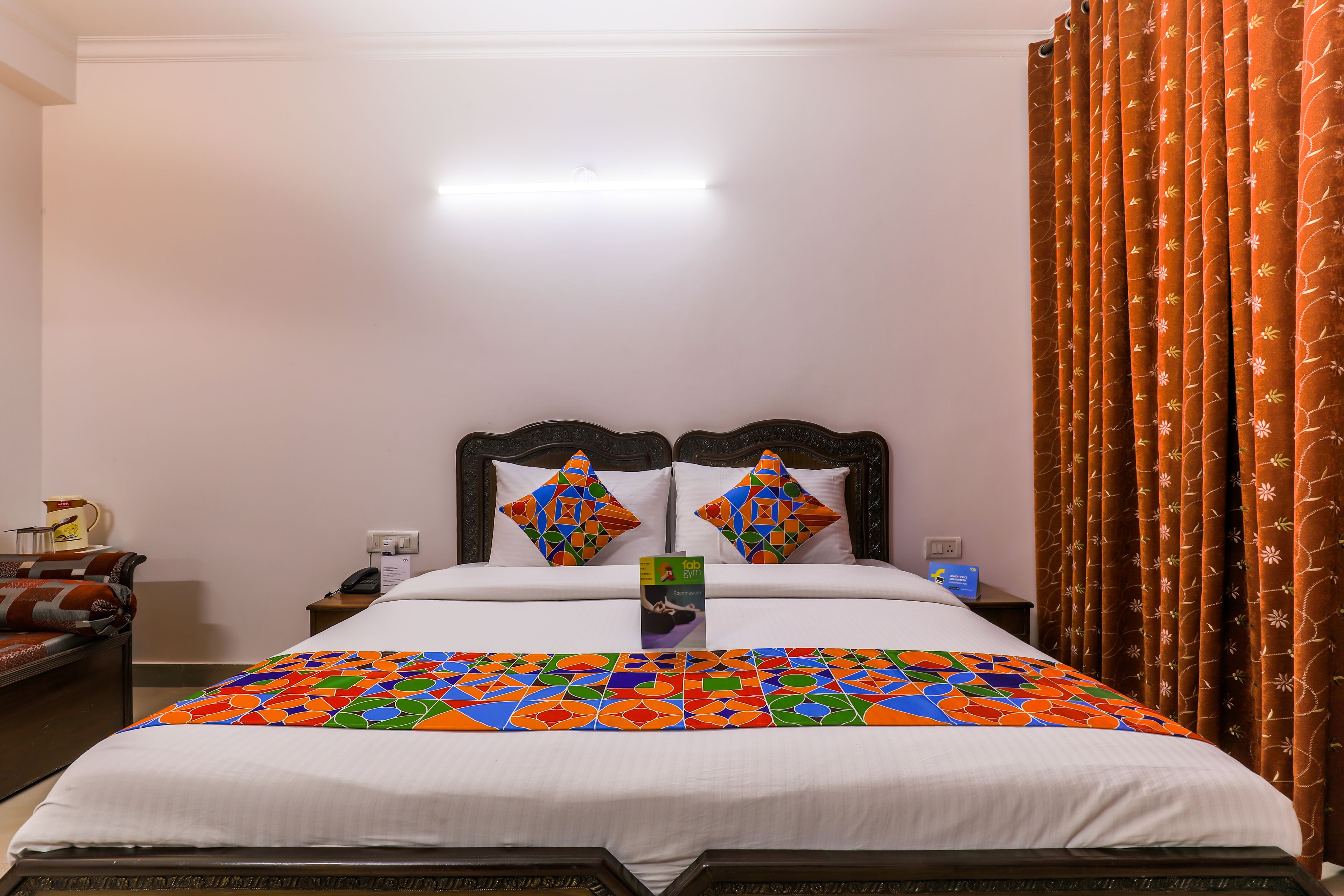 Una habitación de hotel con cama, dos almohadas, una mesita de noche, lámpara y ventana con cortinas.