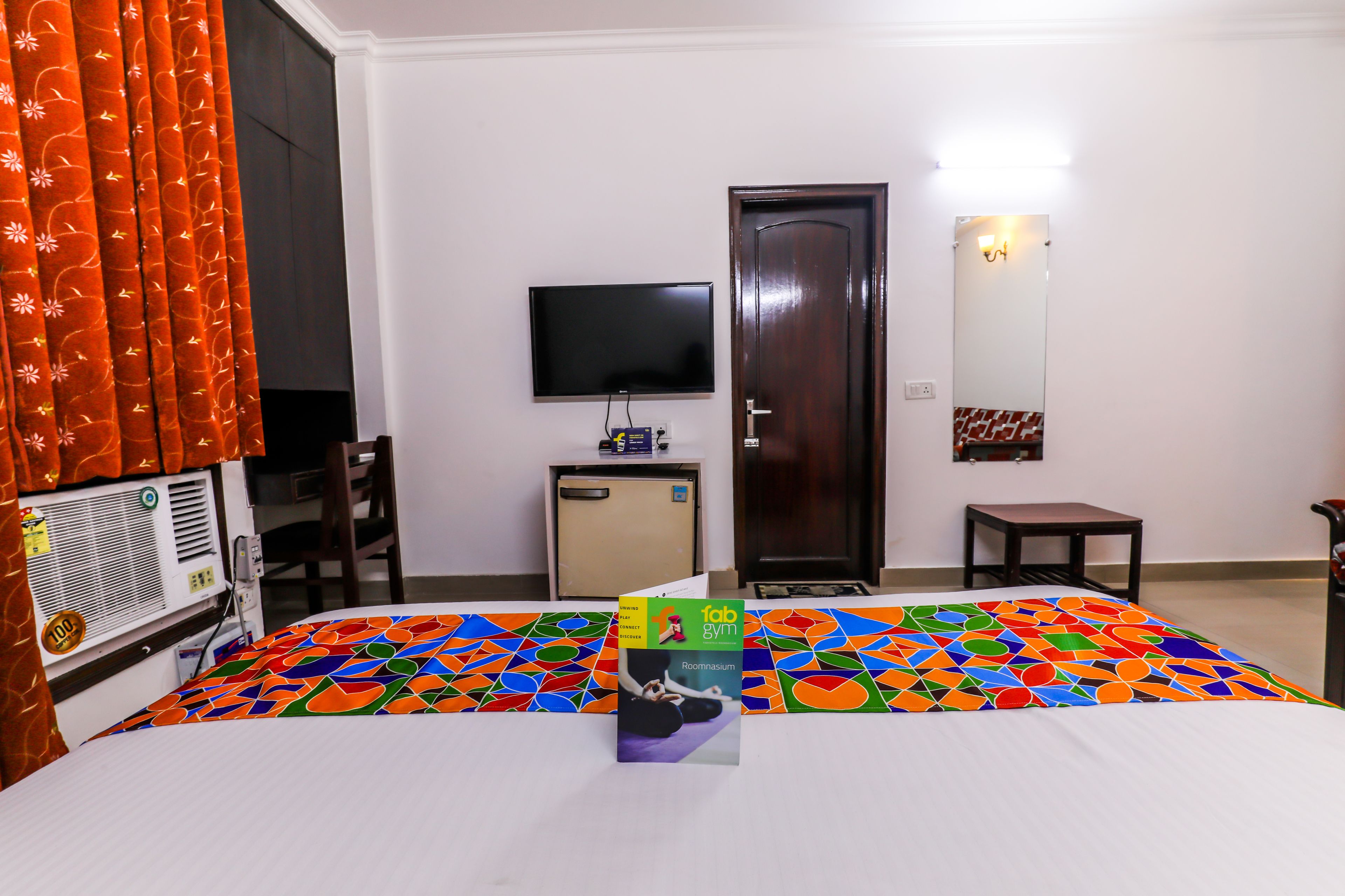 A hotel room with a bed, a TV, a small table, a mirror, and a door.