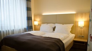 Una habitación de hotel con una cama, dos mesitas de noche y una mesita auxiliar.