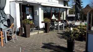 Un restaurante con terraza, mesas, sillas y plantas en macetas.