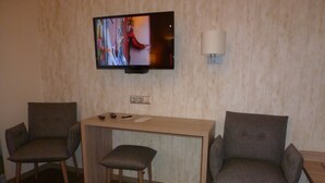 Habitación de hotel con una televisión montada en la pared, un escritorio con dos sillas y una cama con cubrecama rojo.