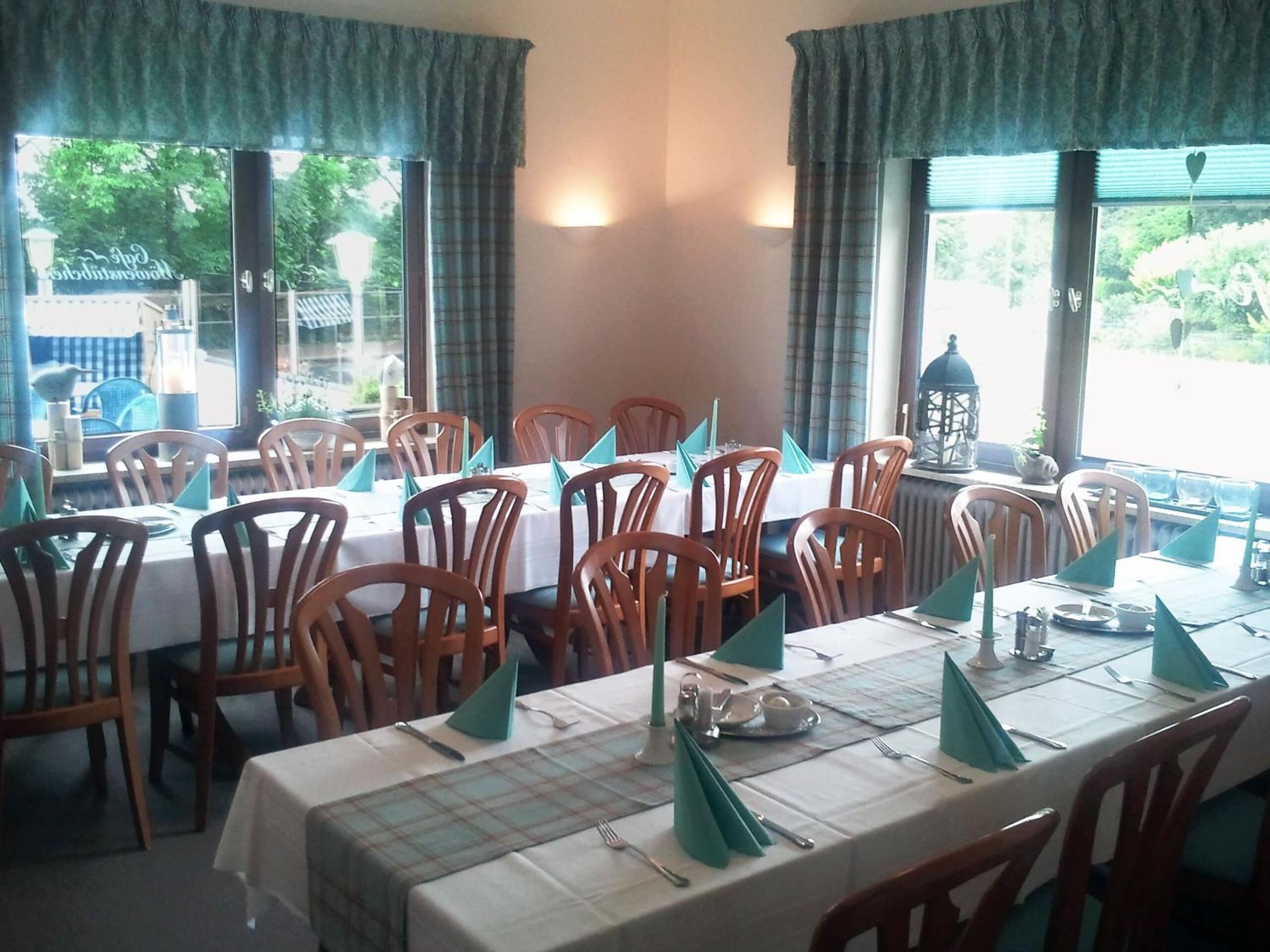 A dining area with tables set for four, wooden chairs, and a view of the outside through large windows.