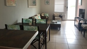 A living room with a dining table, two sofas, a TV, and a ceiling fan. - Beautiful Beach Apartment at Sandy Beach, Rincon (Rincon)