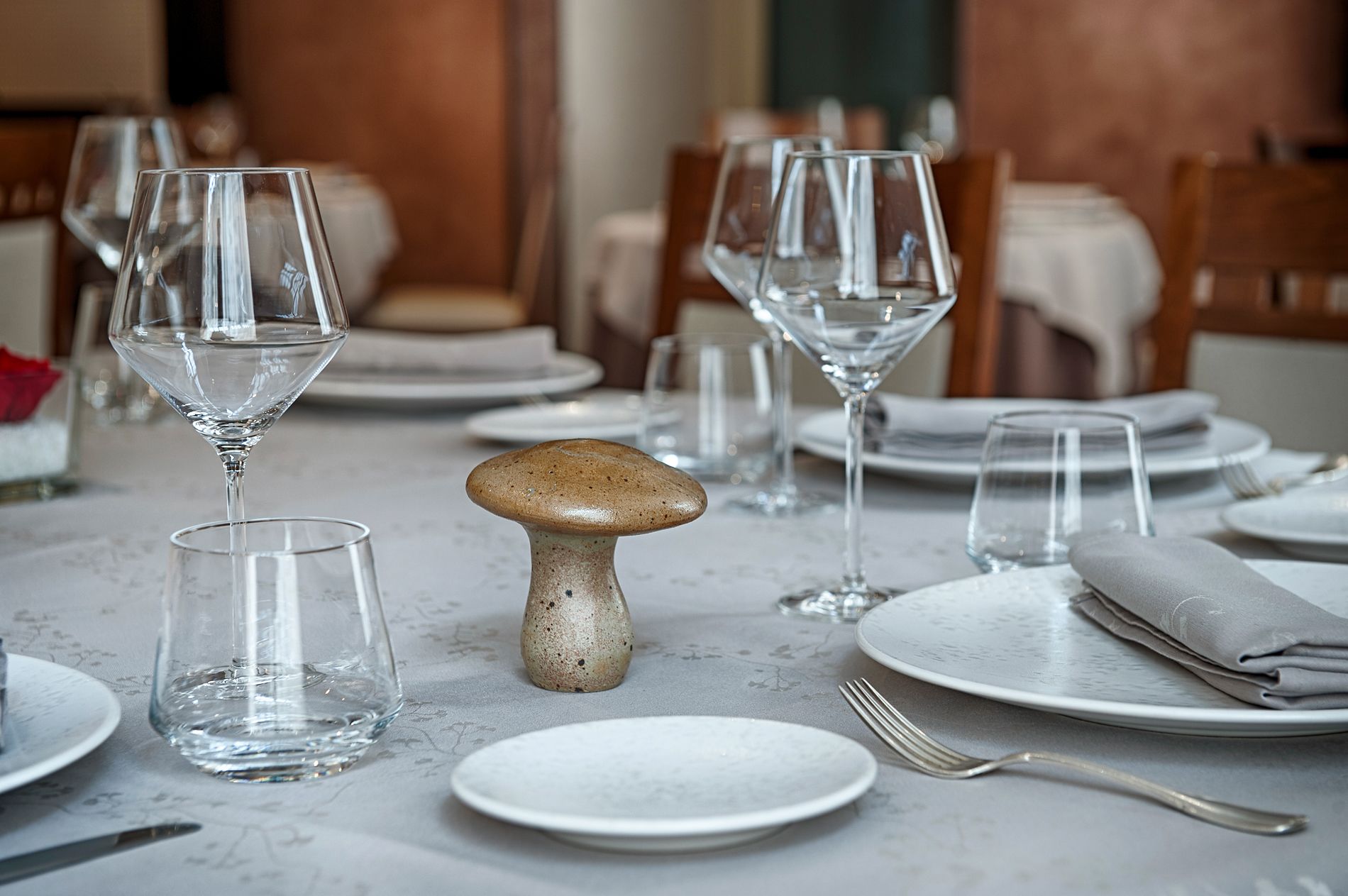 Una mesa de comedor dispuesta con cristalería transparente, un original centro de mesa con setas y servilletas dobladas con esmero.