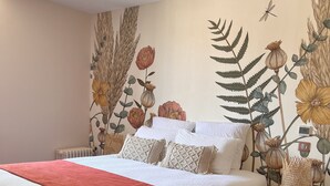 Een slaapkamer met een bed, een rode deken, een gele stoel en een muurschildering van bloemen en bladeren.