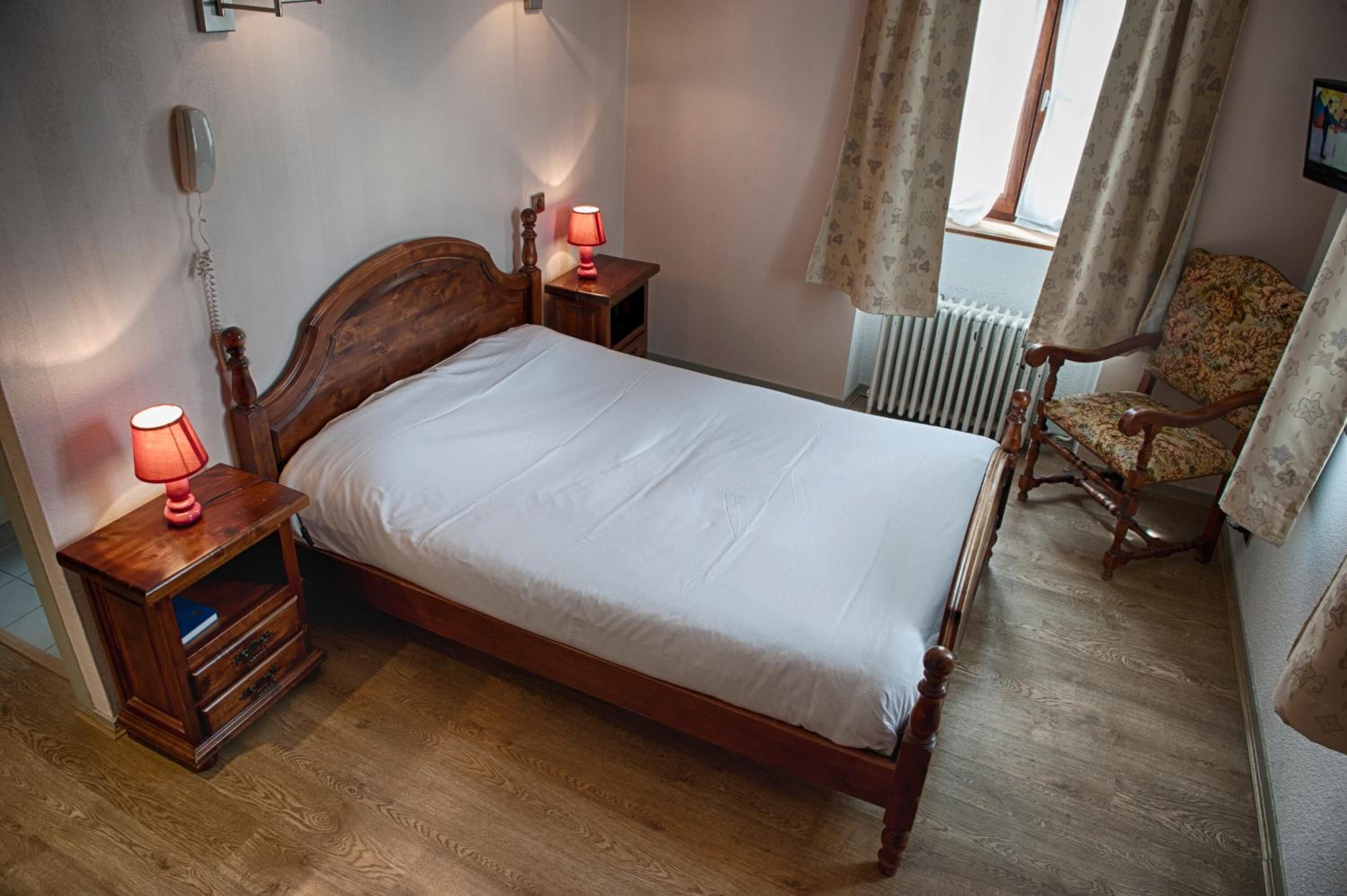 Un dormitorio con una cama de madera, dos mesitas de noche con lámparas, una silla y un radiador.