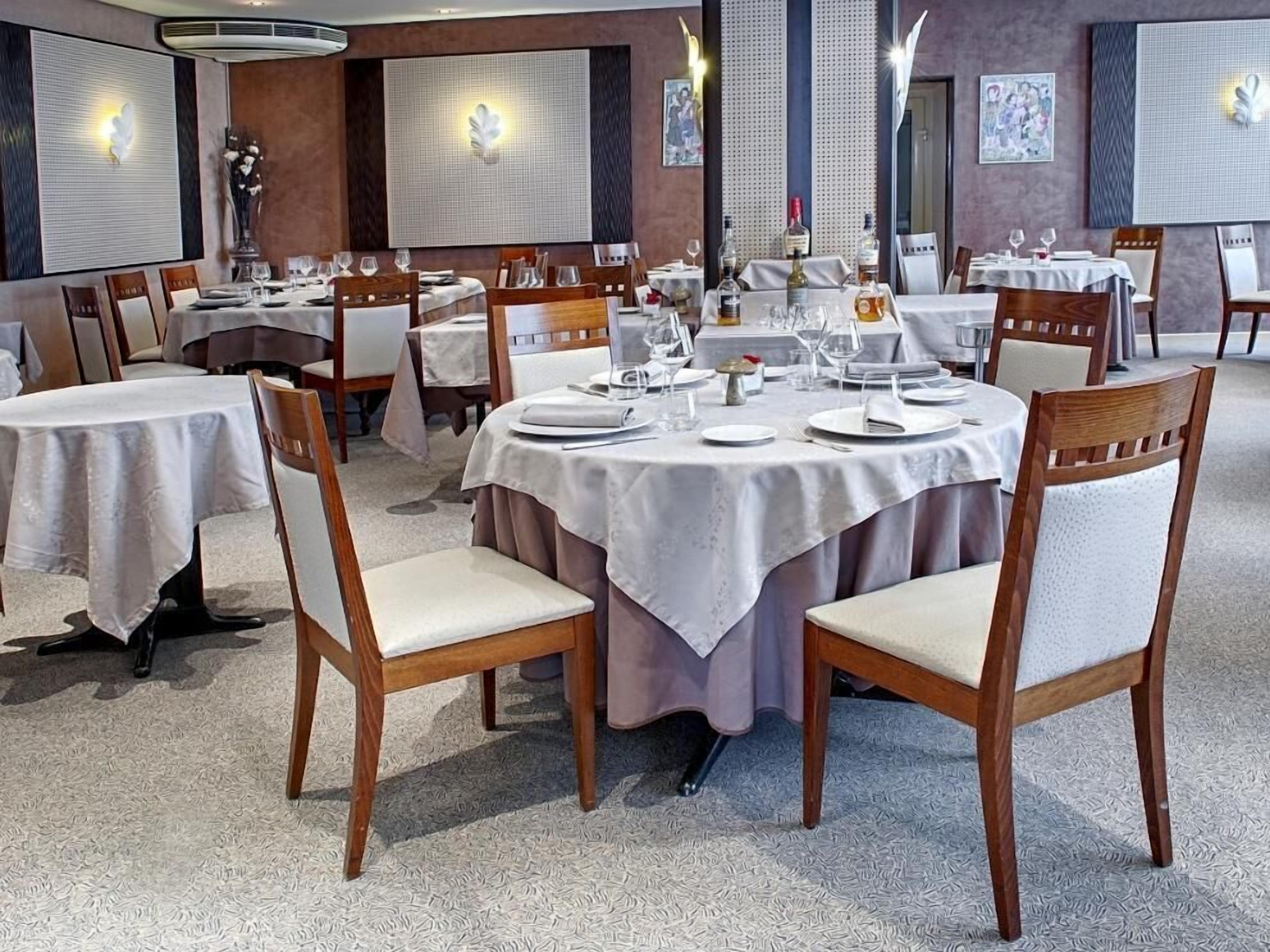 A restaurant with round tables set for dining, featuring white tablecloths and wooden chairs.