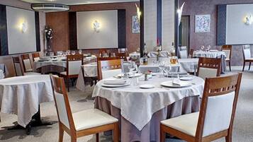 A restaurant with round tables set for dining, featuring white tablecloths and wooden chairs.
