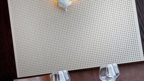 Een eettafel gedekt met borden, bestek en glazen, met een decoratief paneel aan de muur en een kleine steen op de achtergrond.