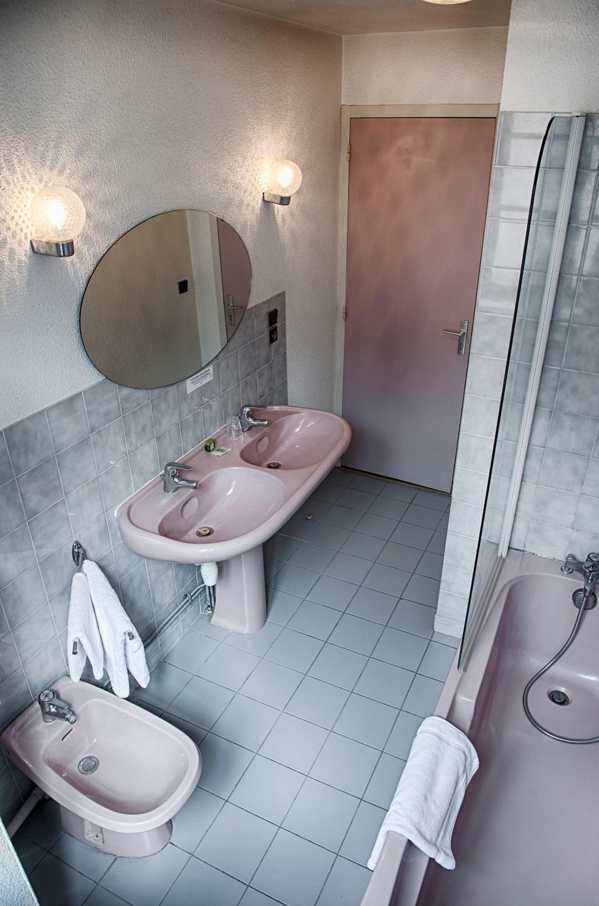 Un baño con un lavamanos rosa, un bidé, una bañera y un espejo con apliques de pared.